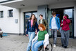 © Halfpoint - Group of teenage students supporting friend in wheelchair in front of school building.