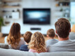 © Mikhail Vorobev - Family of five sitting closely together on a comfortable sofa enjoying a movie in a cozy living room with a blurred television screen in the background