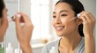 © Luan - A young Asian woman applying facial serum in front of a mirror with a smile