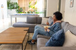 © wavebreak3 - African American woman sitting on sofa in living room, holding popcorn bowl and remote, copy space
