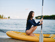 © SHOTPRIME STUDIO - A woman sits cross-legged on a bright yellow kayak by calm water, gripping a paddle as the sun casts soft light, inviting a moment of quiet adventure.