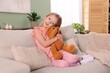© New Africa - Little girl hugging her teddy bear on sofa at home