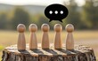 © joeycheung - Five wooden figures stand on a stump with a speech bubble above them.