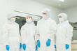 © buritora - Male and female staff working in a manufacturing plant, wearing protective suits and cleanroom wear.