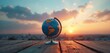 © miss irine - Globe rests on wooden table at sunset. City skyline blurred in background. Sky shows warm colors, clouds drift across. Earth sphere implies global travel or environmental themes.