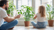 © aMichelle - Young father and little daughter sit on the floor near large green houseplants, watering and caring for indoor plants in a bright modern apartment, promoting family bonding and eco lifestyle
