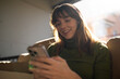 © TrueShot | Westend61 - Smiling woman using smartphone on sofa in bright indoor setting