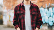 © Bonsales - Person wearing red plaid shirt standing against urban brick wall with graffiti, depicting casual youth fashion