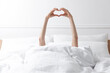 © New Africa - Woman making heart with hands in bed at home, closeup