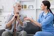 © New Africa - Care worker giving glass of water to senior man with walking cane indoors