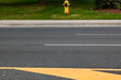 © Chandra - A bright yellow fire hydrant stands on a grassy strip beside a paved road marked with a bold directional arrow