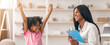 © Prostock-studio - A young girl raises her arms in joy at her achievement while a teacher smiles and holds a clipboard. They are in a classroom filled with learning materials and light colors.