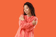 © Pixel-Shot - Young Asian woman hugging himself on orange background