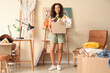 © Pixel-Shot - Young African-American woman with box in room of unwanted stuff