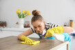 © Pixel-Shot - Pretty young woman in yellow rubber gloves cleaning dining table with rag and detergent