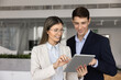 © fizkes - Two smiling colleagues working on task, preparing online presentation, discussing project updates or trends, reviewing AI application or new business tools using digital tablet. Modern tech, teamwork