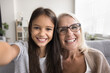 © fizkes - Close up webcam faces, older 55s grandma and 7s grandkid, gazing at camera, make selfie or videocall, record video vlog, looking with joyful expression. Hobby, fun, leisure of multigenerational family