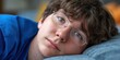 © NovaVision - Close-up portrait of a young person with glasses resting their head on a pillow