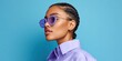 © NovaVision - Stylish young woman with braided hair and purple sunglasses against a blue background