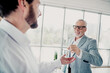 © deagreez - Business partners in a modern office exchange a small bottle during a friendly professional moment