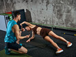 © master1305 - Woman holding side plank position while male coach giving feedback in gym. Concept of performance tracking, fitness assessment session, progress evaluation and personalized training plan