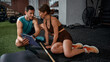 © master1305 - Man and woman discussing workout plan while sitting on gym floor. Concept of fitness consultation advertising, coaching service promotion, branding for wellness business and client onboarding strategy