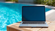© Olha Havelia - Aesthetic shot of a modern laptop with a blank glowing screen resting on a wooden side table next to a turquoise swimming pool, Digital Nomad concept, sharp focus on the laptop's m