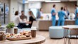 © Justlight - Shared table in a clinical break room with focused hands stacking fresh snacks and coffee cups surrounded by outoffocus seating and medical staff lockers.