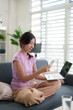 © Pichsakul - Asian adult woman multitask work online home office using laptop smartphone for digital communication connectivity in cozy living room