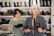 © JackF - Elderly female friend strongly recommends her young colleague to pay attention to classic hills shoes made in light leather. Female clients want buy and choose woman dress shoes