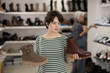 © JackF - Female customer is standing next to shelf in stores sales area. She picks up shoes, looks at and studies material and quality of product, decides to buy shoes