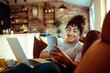 © Davor - Young woman using smartphone and laptop at home