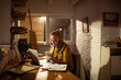 © Davor - Smiling young woman using smartphone and laptop in home office at night