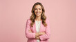 © Ahsan - A cheerful, attractive young woman with flowing natural hair and a confident smile stands with crossed arms in a stylish pink blazer a plain pink background.