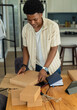© wavebreak3 - African American man in twenties leaning over table in kitchen wearing beige shirt packing boxes