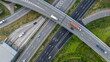 © Fahroni - Aerial top view of highway junction interchange road. Drone view of the elevated road, traffic junctions, and green garden. Transport trucks and cars driving on highway. Infrastructure in modern city.
