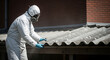 © Fajar - asbestos removal professional in protective suit handling hazardous asbestos sheets on an old roof emphasizing health safety.