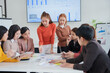 © aekachai - A group of young professional women are deeply engaged in a meeting around a table filled with charts and data. The team leader is explaining the strategy, showcasing a collaborative and dynamic workp