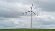 © Volha - Wind turbine rotating on green field under cloudy sky.