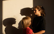 © Anna - Silhouettes of faces and shadows cast by sunlight on the wall by an older sister and younger brother. Sibling support and closeness. The younger generation