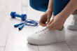 © New Africa - Woman tying shoelace of sneakers, skipping rope, dumbbell and water indoors, closeup