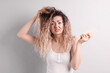 © New Africa - Unhappy woman trying to brush her tangled hair on light grey background
