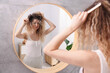 © New Africa - Unhappy woman trying to brush her tangled hair near mirror in bathroom