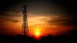 © FaizulPe - A dramatic sunset silhouettes a tall telecommunication tower against a vibrant orange and yellow sky, symbolizing modern connectivity.