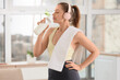 © Pixel-Shot - Sporty young woman with headphones and towel drinking protein shake at home