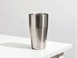 © LI - A sleek modern stainless steel tumbler stands alone on a clean white surface against a minimalist grey background with soft natural lighting.
