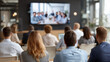 © Joseph - Audience of corporate employees watching virtual global town hall meeting on large screen. Large diverse business team attending remote video conference or webinar presentation.