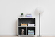© Pixel-Shot - Shelf unit with folded clothes and lamp near light wall in room