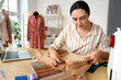 © Pixel-Shot - Female tailor working with pattern and cloth at table in atelier