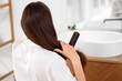 © Pixel-Shot - Young brunette woman brushing hair in bathroom, back view